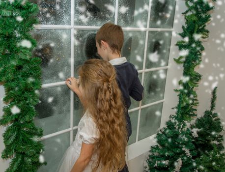 Smiling sister and brother in winter studio looking at snowy window