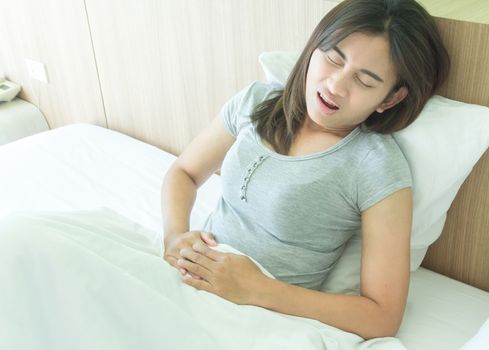 Closeup woman hand holding abdominal with stomach ache lying on bed, health care and medical concept