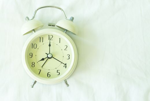 Closeup top view alarm clock on white bed in bedroom for wake up time concept 