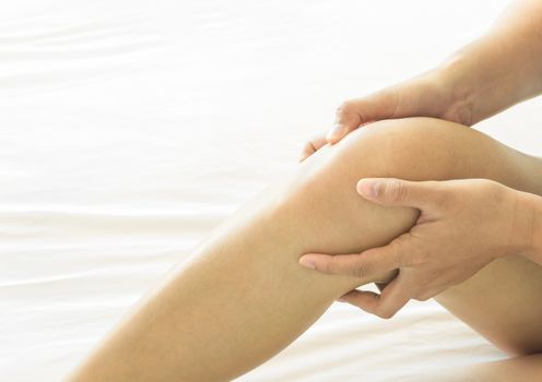 Closeup woman hand holding knee with pain on bed, health care and medical concept