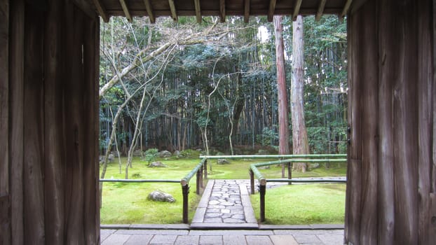 Wooden framed view on a path through a Japanese garden with trees and green grass on a bright day.