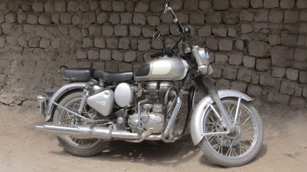 Old silver motorcycle is parking in front of a stone wall during the day.