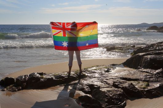 On November 15 Australia voted yes to Marriage Equality.  A woman holding an Australian flag in rainbow colours by the ocean