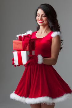 Beautiful young woman in Santa dress celebrating Christmas holding gift boxes