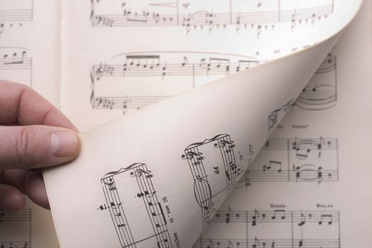 a hand turns a page of the musical score