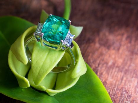 Closeup green gem ring with white diamond wear with petal of ylang-ylang flower on green leaf