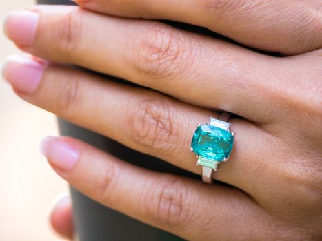 Closup female hand holding coffee cup and wearing green gem ring with white diamond on finger