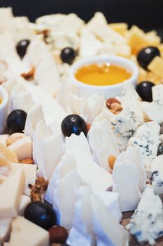 Cheese plate. Assortment of cheese with walnuts and honey from honey dipper on white wood serving board over white concrete texture background. Top view with space. Appetizer theme.