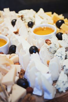 Cheese plate. Assortment of cheese with walnuts and honey from honey dipper on white wood serving board over white concrete texture background. Top view with space. Appetizer theme.