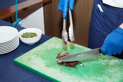 Young white chef in kitchen interior. Man marinating beef steak on a tray. Meat ready for the grill and serve. Only hands.