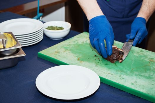 Young white chef in kitchen interior. Man marinating beef steak on a tray. Meat ready for the grill and serve. Only hands.