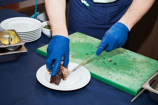 Young white chef in kitchen interior. Man marinating beef steak on a tray. Meat ready for the grill and serve. Only hands.