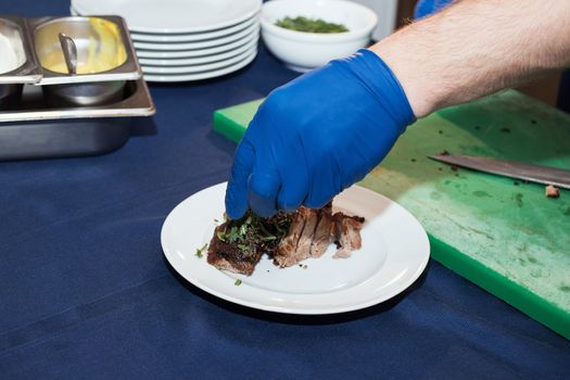 Young white chef in kitchen interior. Man marinating beef steak on a tray. Meat ready for the grill and serve. Only hands.