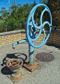 Blue water well pump, with wheel, on summer sun