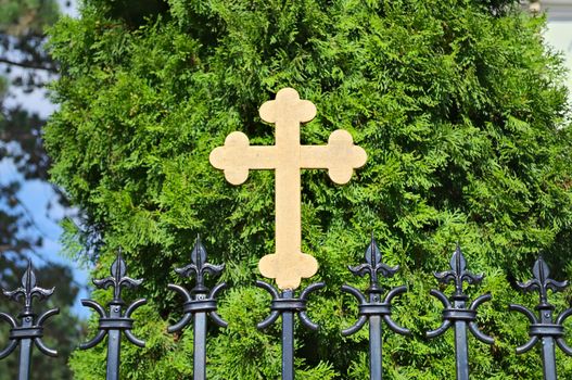 Metal cross on monastery fence, in front of tree