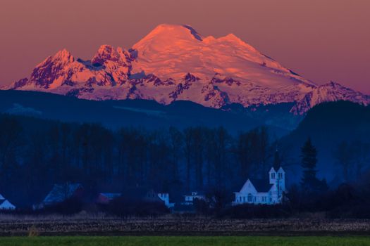Sun setting on Mount Baker from Skagit Valley with church in foreground