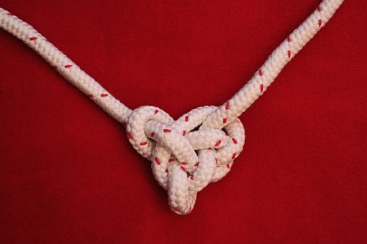 knot in heart shape, White rope on red background. copy space