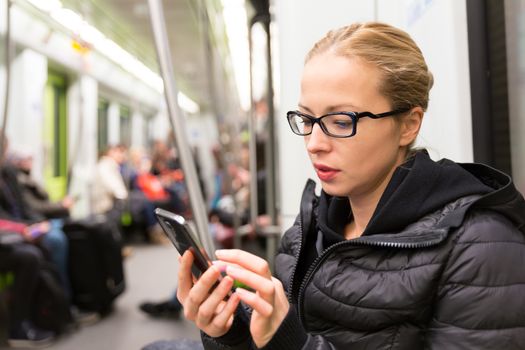 Young girl reading from mobile phone screen while traveling on metro. Wireless internet on public transport concept.