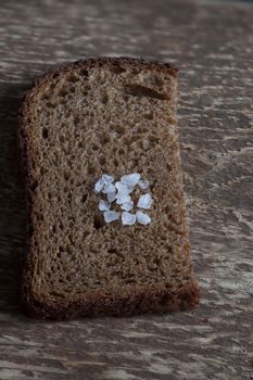 piece rough rye bread with coarse salt on a wooden background, macro shot