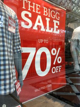 Mens fashion boutique Sale Sign showing markdowns up to 70% in shop front window with mannequins