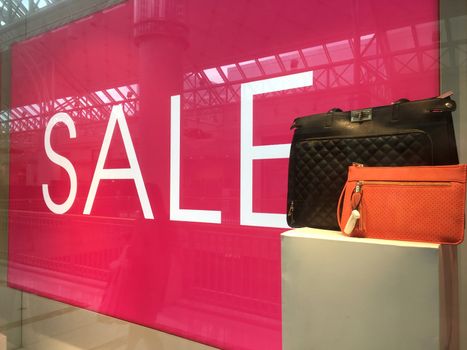 Large glossy Sale Sign and handbags on display in shop front window