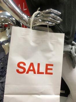 Mannequin holding a sale paper shopping carry bag