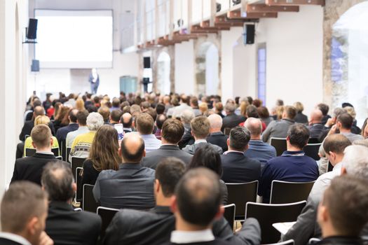 Speaker giving a talk in conference hall at business event. Audience at the conference hall. Business and Entrepreneurship concept. Focus on unrecognizable businessman in the audience.