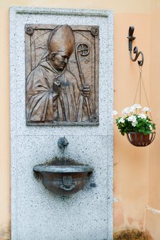 Tape in bronze of the Pope Jean-Paul two hang on a plate of granite with a sink and a pot of flowers