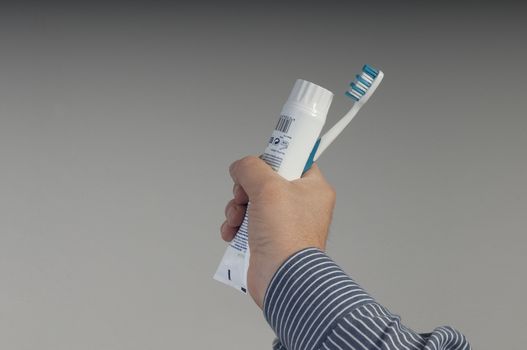 a tube of toothpaste and a toothbrush in hand