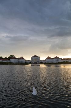 Dramatic scenery of Nymphenburg palace in Munich Germany. Sunset after the sorm. White swan diving in pond in front of the palace.