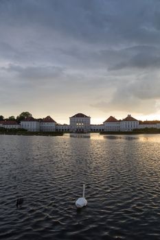 Dramatic scenery of Nymphenburg palace in Munich Germany. Sunset after the sorm. White swan swimming in pond in front of the palace.