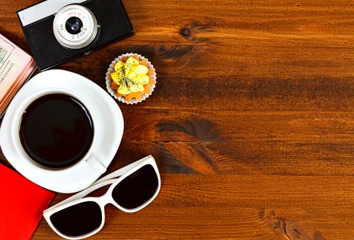 Retro photo camera, coffee cup, passport, sunglasses and cupcake on brown wooden table with space for text, top view.