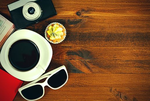 Retro photo camera, coffee cup, passport, sunglasses and cupcake on brown wooden table with space for text, top view.