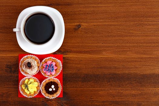 Cup of tea or coffee and four cupcakes on brown table. Top veiw