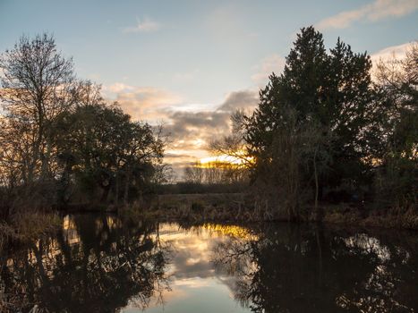beautiful sun set autumn light sky over river trees reflections water surface; essex; england; uk