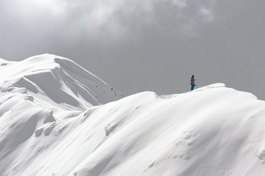 A stranded man on the snowy ridge of a mountain holding a cell phone trying to call