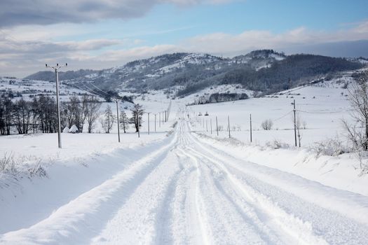 A thick layer of snow fallen over a road with visible vehicle tracks and a nice perspective  in a winter landscape