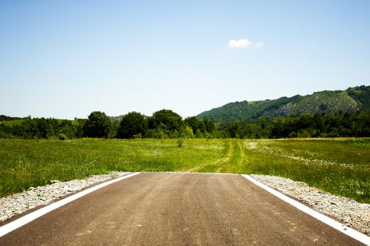 Paved road ending abruptly in the middle of a green plain with some trails ahead