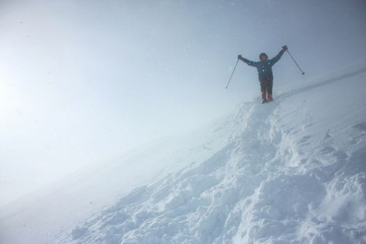 A mountaineer equipped with snow shoes and ski poles saluting when walking down a snowy track on a slope in a strong snow storm with snow flakes everywhere
