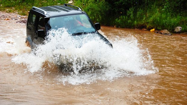 Off road vehicle crossing a deep stream of muddy water with big splash on the hood