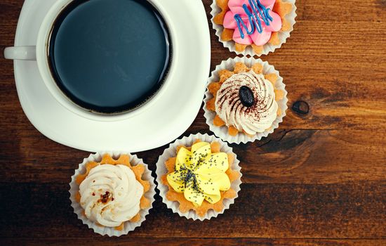 Closeup shot of small cup of coffee with colorful cupcakes. Flat lay style