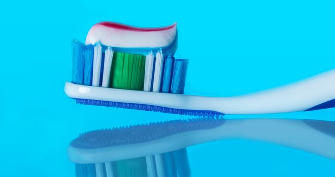 toothbrush with paste on a blue background with reflection