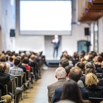 Speaker giving a talk in conference hall at business event. Audience at the conference hall. Business and Entrepreneurship concept. Focus on unrecognizable man in the audience.