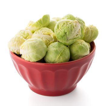 Fresh brussels sprouts on red ceramic bowl isolated on white background.