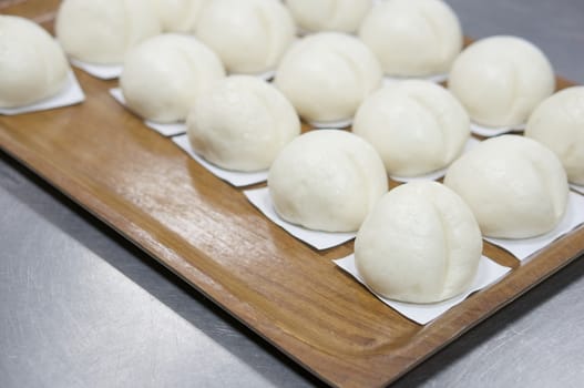 Close up steamed bun or dim sum on white paper in brown wooden tray have aluminium table as background at restaurant kitchen with copy space. Food and healthy concept photography.