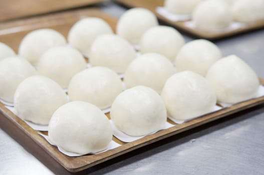 Close up steamed bun or dim sum on white paper in brown wooden tray have aluminium table as background at restaurant kitchen. Food and healthy concept photography.
