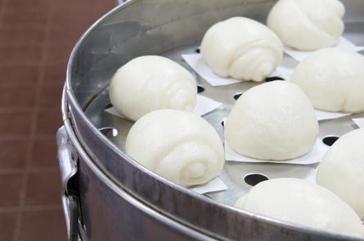 Steamed bun or dim sum on white paper in big aluminium steamer at restaurant kitchen with brown tile on floor as background and copy space. Food and healthy concept photography.