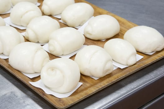 White steamed bun or dim sum on white paper in brown wooden tray have aluminium table as background at restaurant kitchen. Food and healthy concept photography.