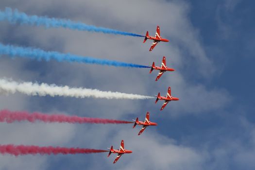 Royal air force red arrows in part of an air display flying in formation with red white and blue smoke trails in England.