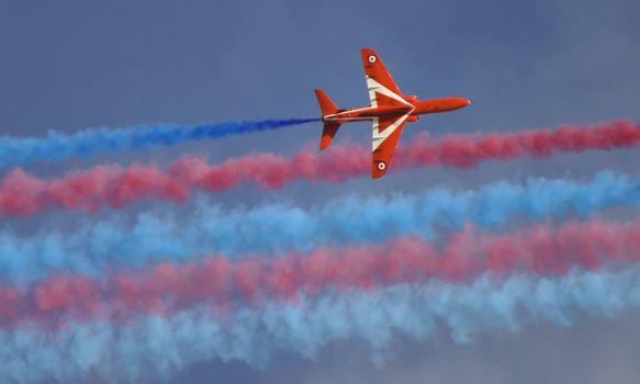 Royal air force red arrow with smoke trails part of an air display flying overhead in england.